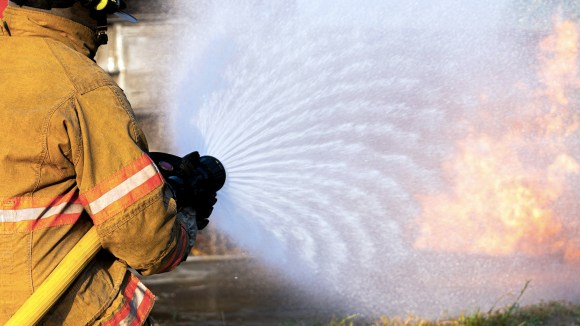 Network hose: Managing uncertain network demand. Image shows Rear View Of Firefighter high pressure spraying water to stop fire.